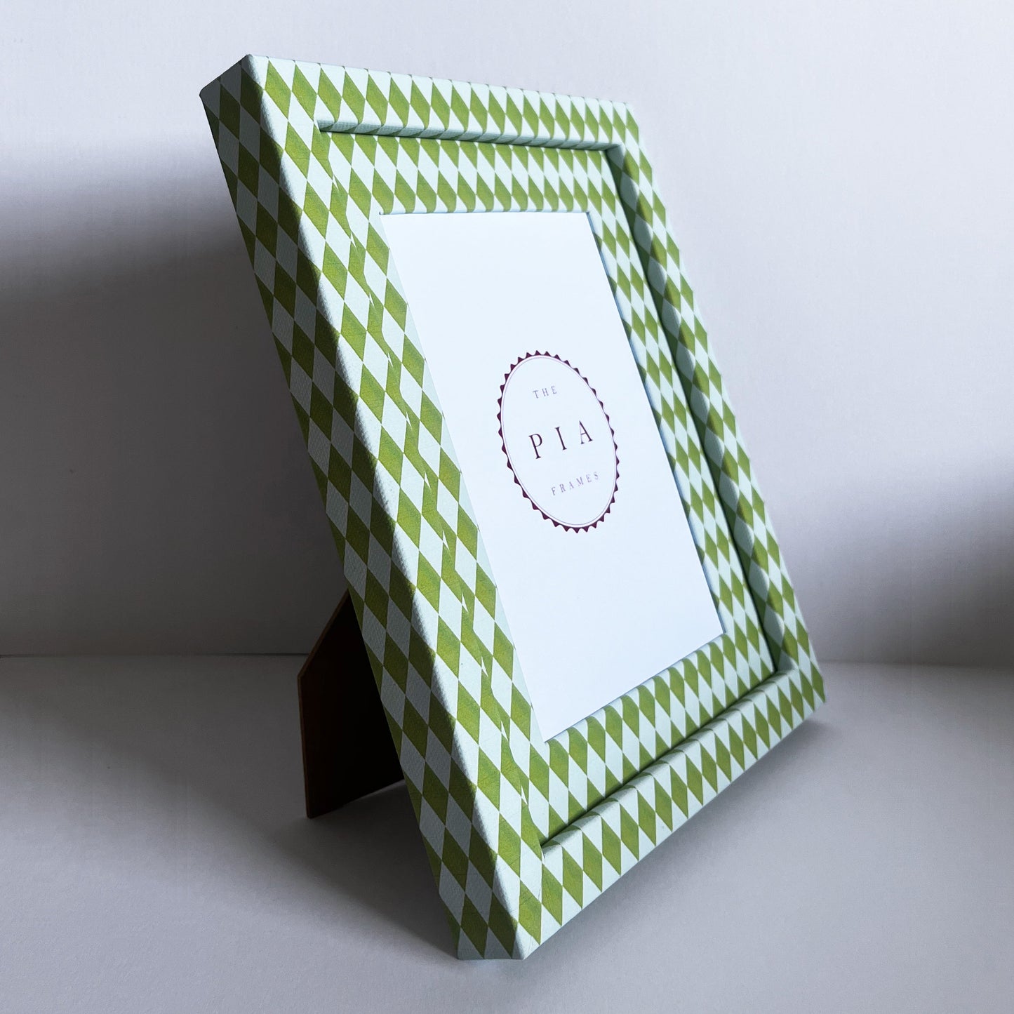 Green and blue decorative picture frame with a harlequin pattern, stood up, in front of a white background 