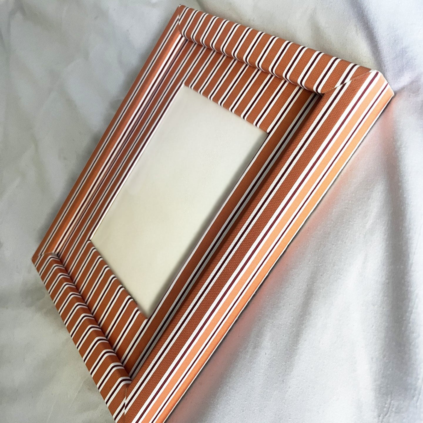 Rectangular picture frame with orange striped design on a white fabric background