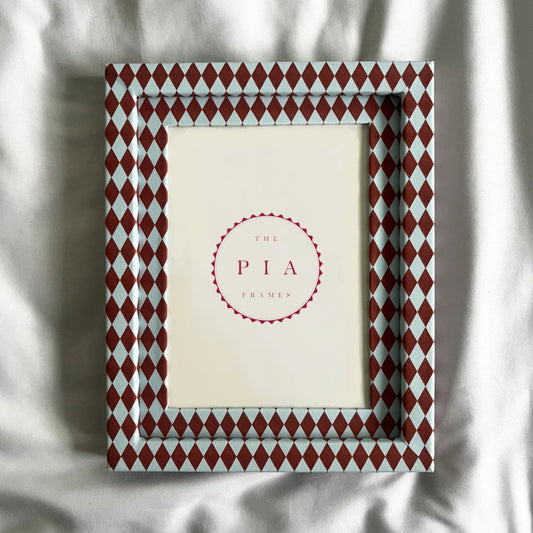 Decorative picture frame with red and blue diamond pattern on a white fabric background