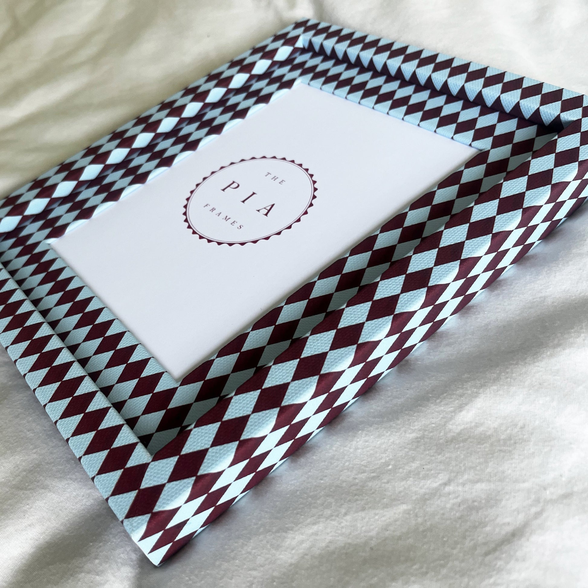 Side view of burgundy and blue harlequin fabric frame, on a white linen fabric, showcasing the depth of the frame