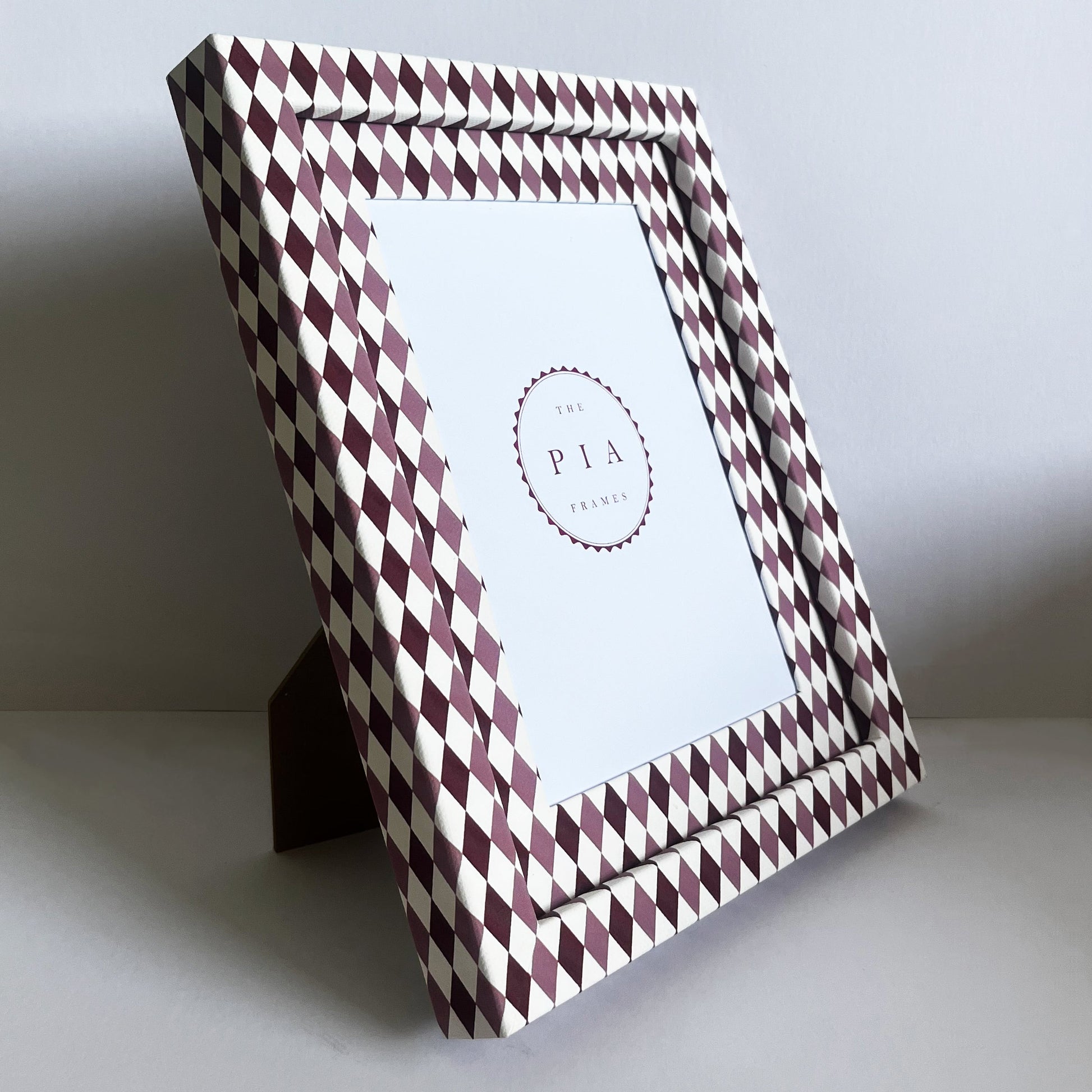 Decorative photo frame with a burgundy and blush harlequin fabric frame standing on its stand, in front of a white background
