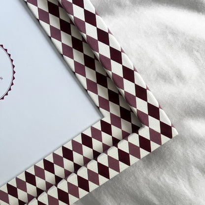 Close up of burgundy, blush and white harlequin fabric frame, on a white linen fabric, showcasing the texture