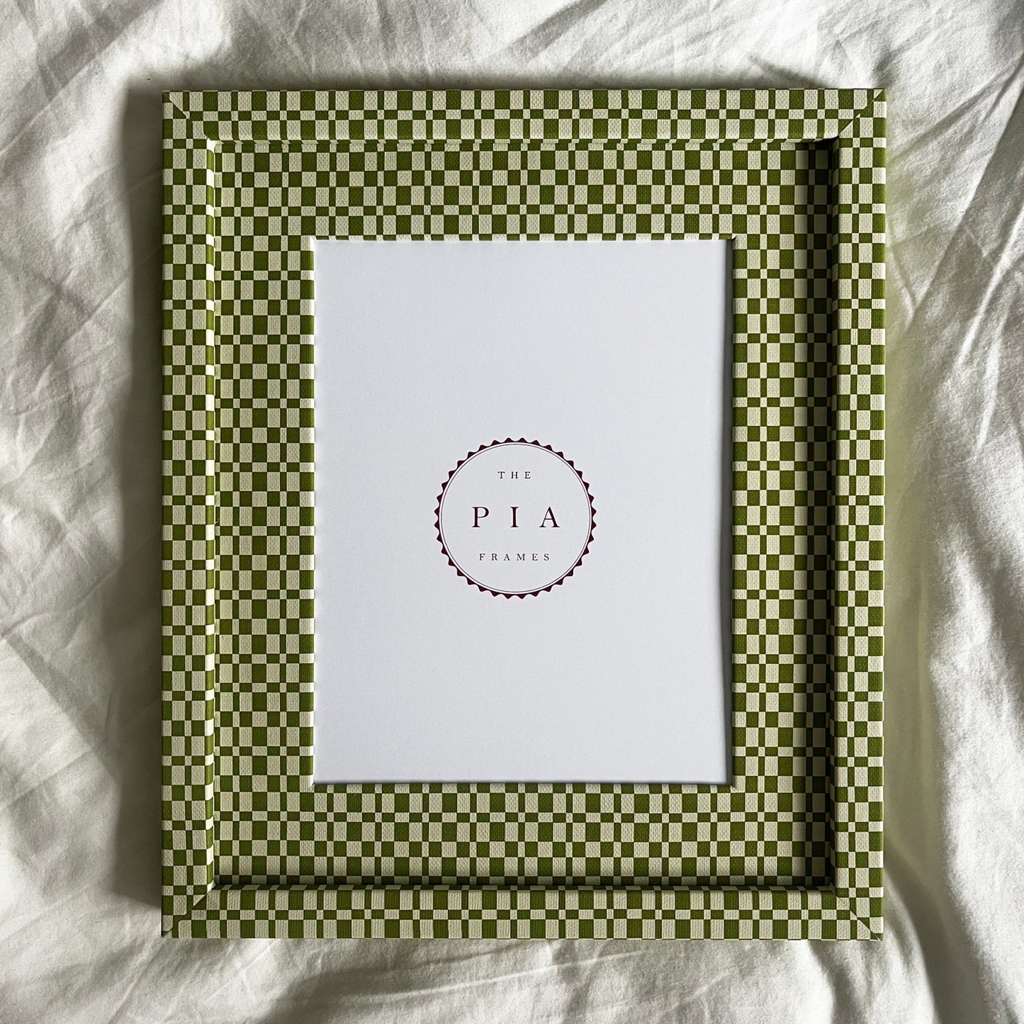 Handmade green checkered frame with a white center on a white fabric background