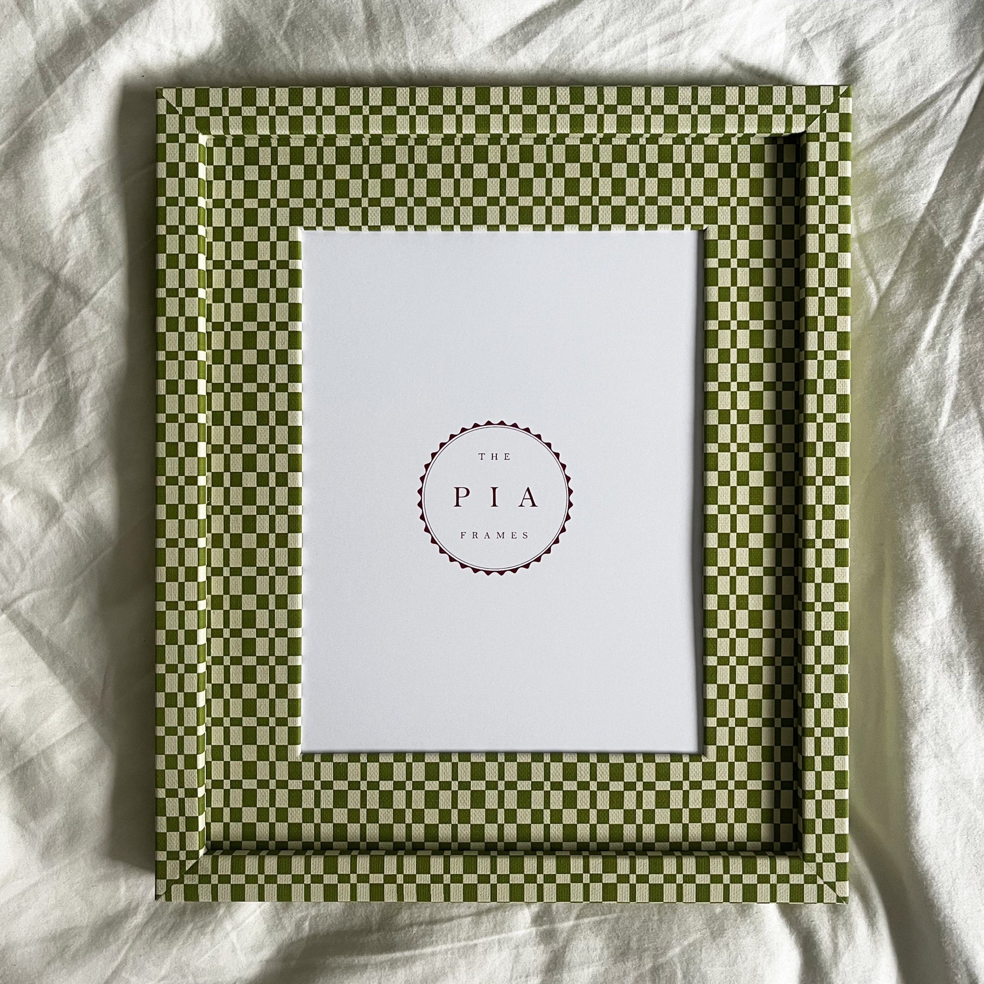 Handmade green checkered frame with a white center on a white fabric background