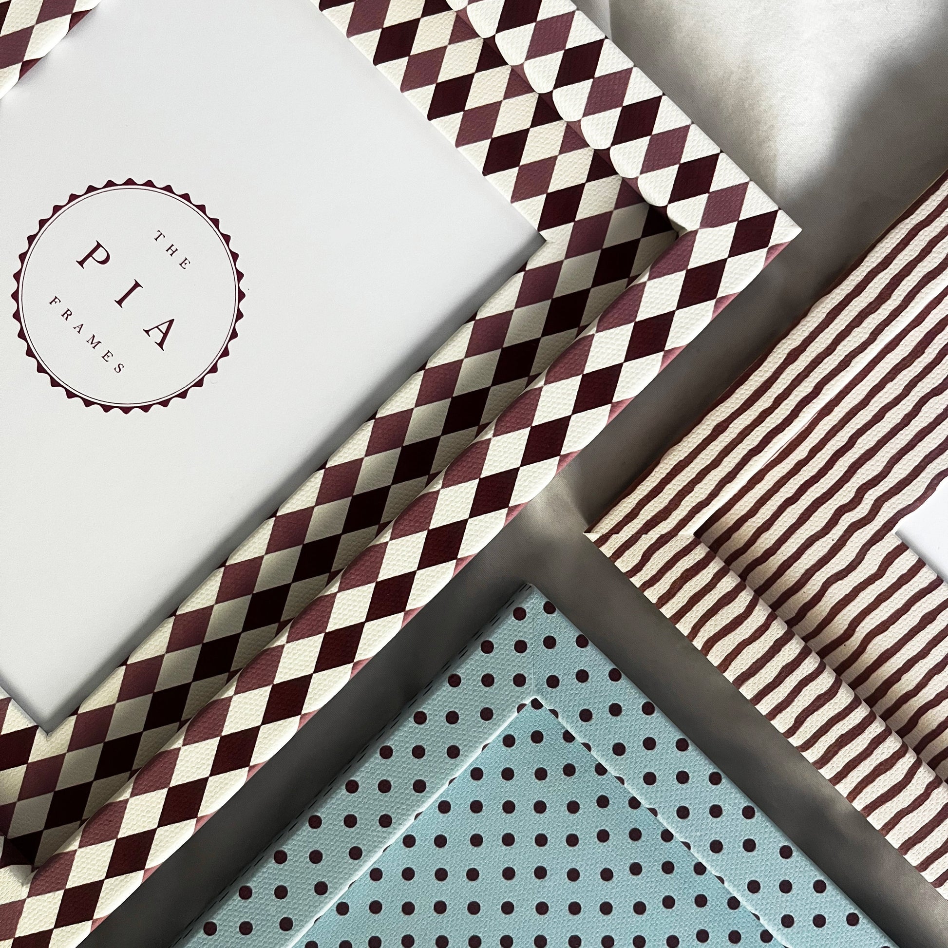 Three fabric wrapped picture frames, with harlequin, stripe and polka dot patterns arranged on fabric