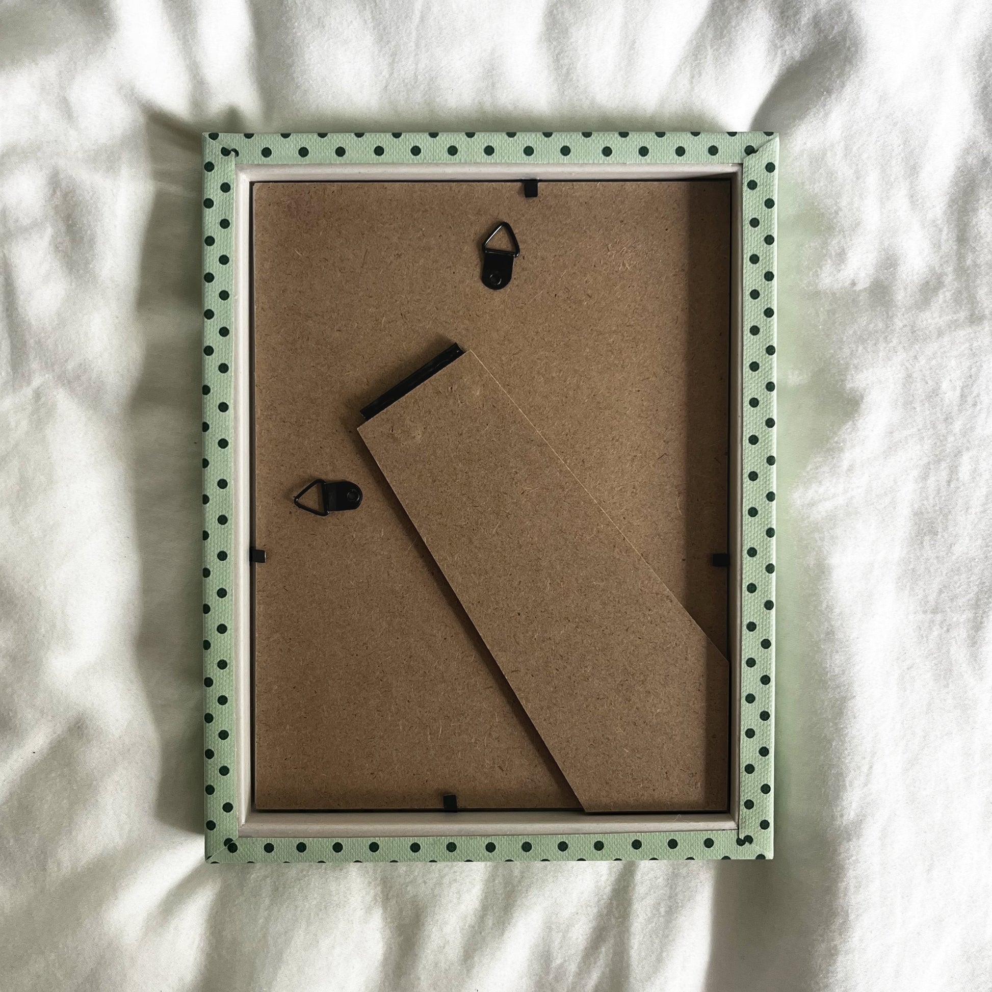 Back view of handmade mint green and jade Pembroke polka dot fabric picture frame, showing wall fittings and frame structure