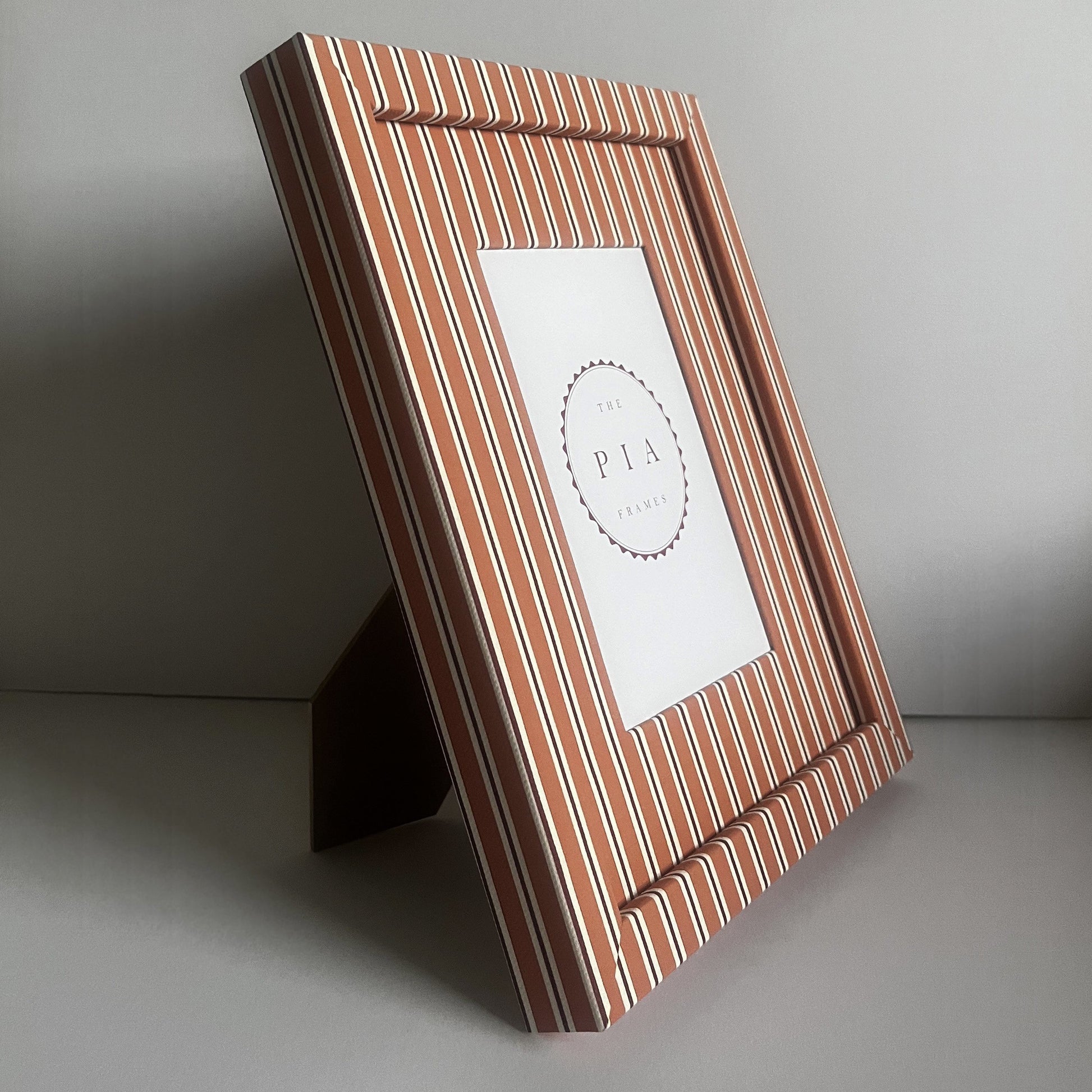 Handmade orange and burgundy stripe picture frame standing on a stand, showcasing the frame’s design and depth