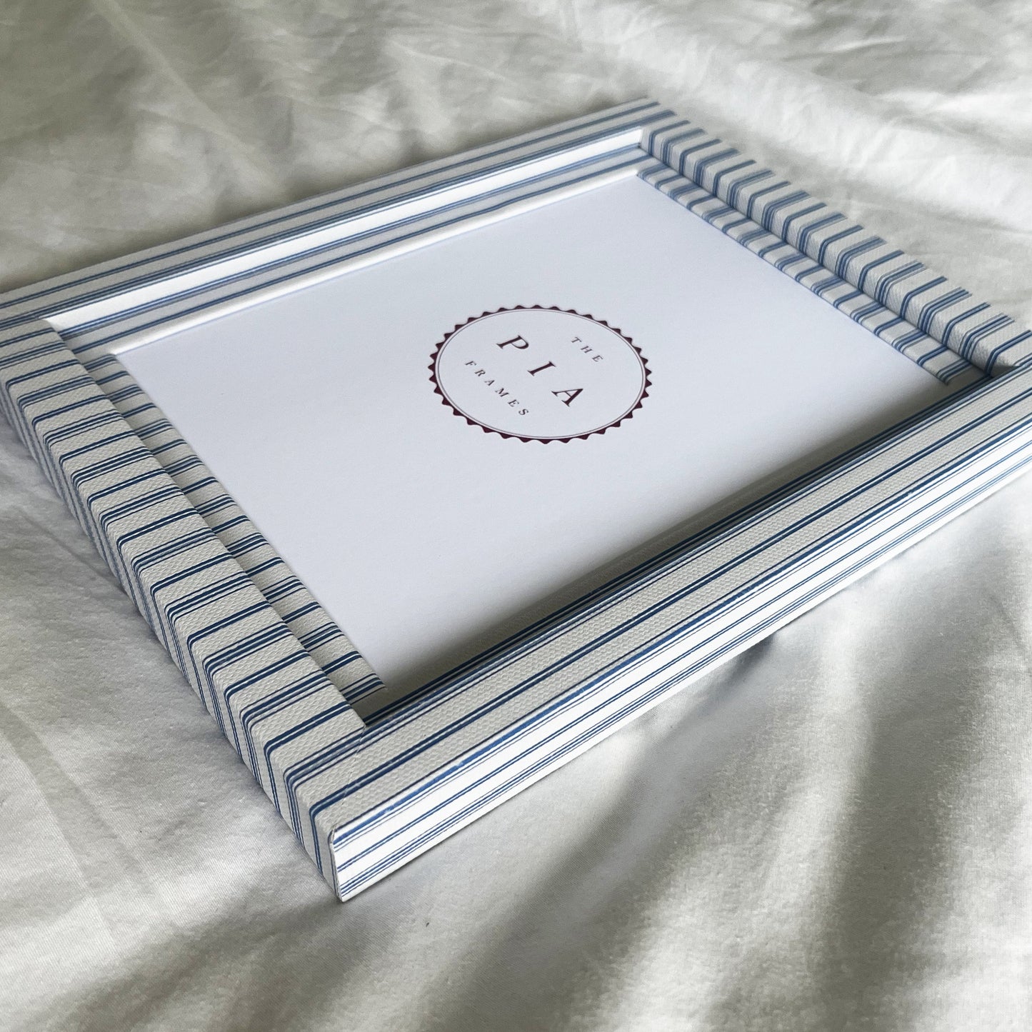 Side view of rustic blue striped picture frame on a white linen background, showcasing the frame’s depth and design