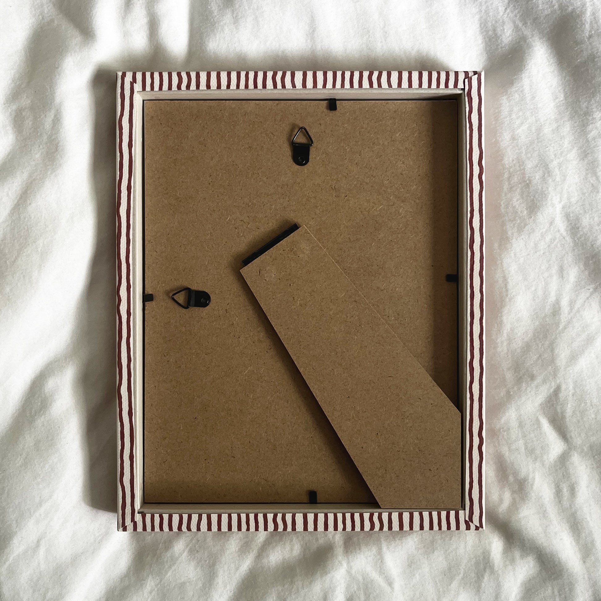 Back view of terracotta and beige striped picture frame, showing wall fittings and frame structure