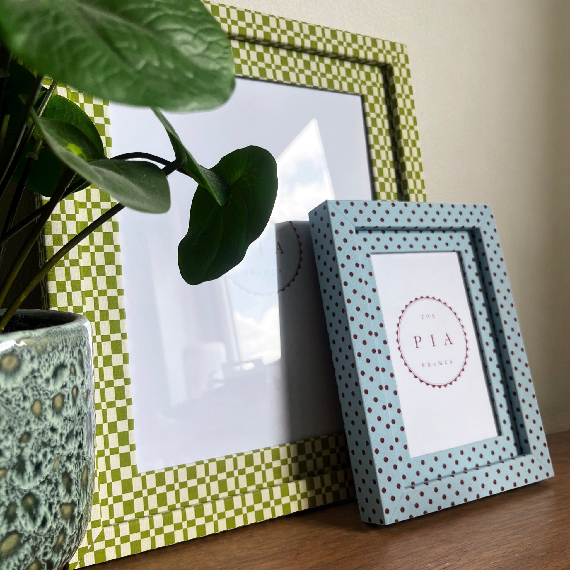 Two decorative fabric picture frames on a wooden surface with a plant in the background.
