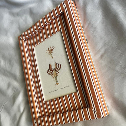 Side angle of hermit crab artwork showing the artisanal Tangerine (orange) & Burgundy (red) Seaside Stripe frame design