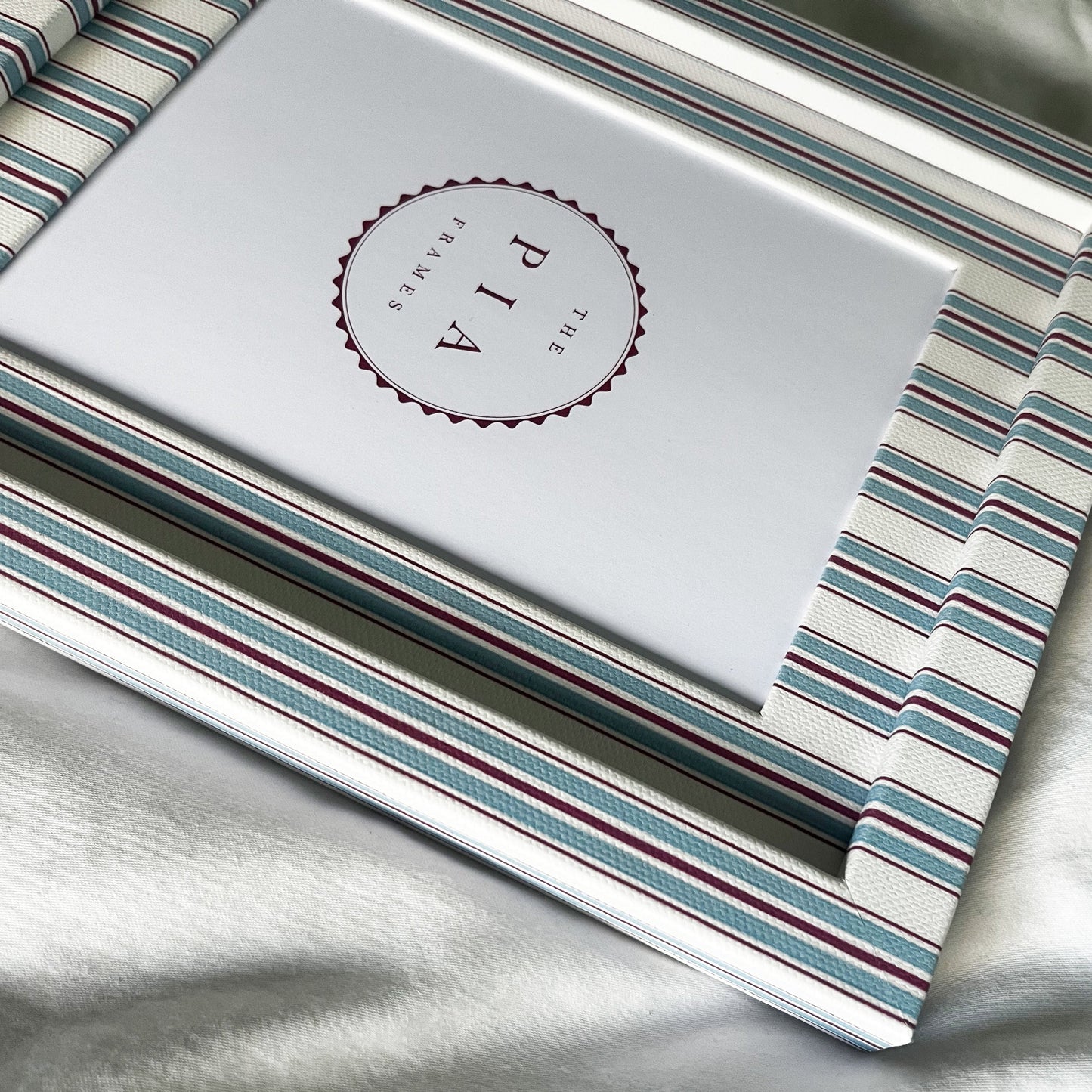 side view of cotton wrapped blue and red striped picture frame on a white linen background