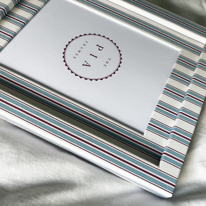 side view of cotton wrapped blue and red striped picture frame on a white linen background